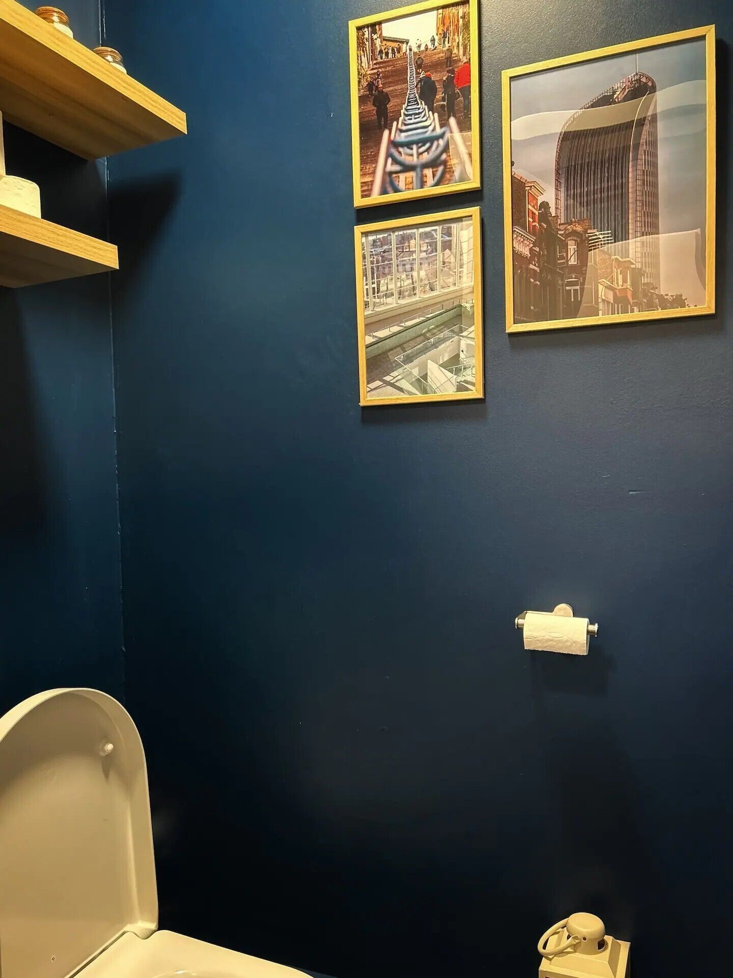 Een badkamer met een blauwe muur, een toilet en drie ingelijste afbeeldingen van architecturale bouwwerken.