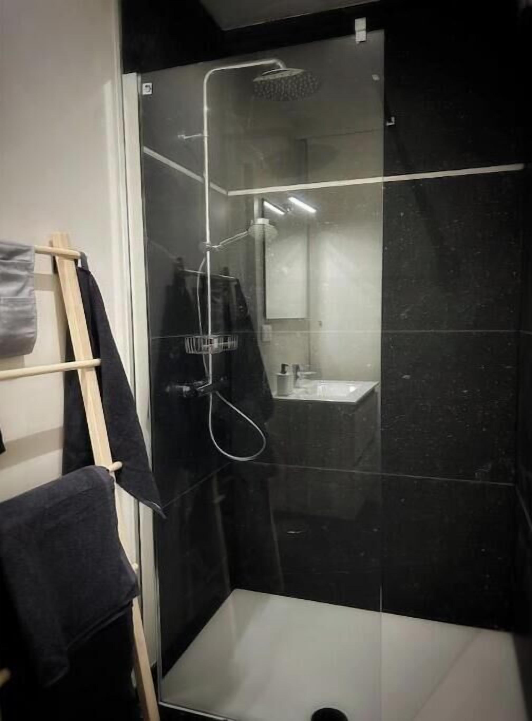 Une salle de bain moderne avec une douche à parois de verre, un porte-serviettes en bois et un espace lavabo bien visible.