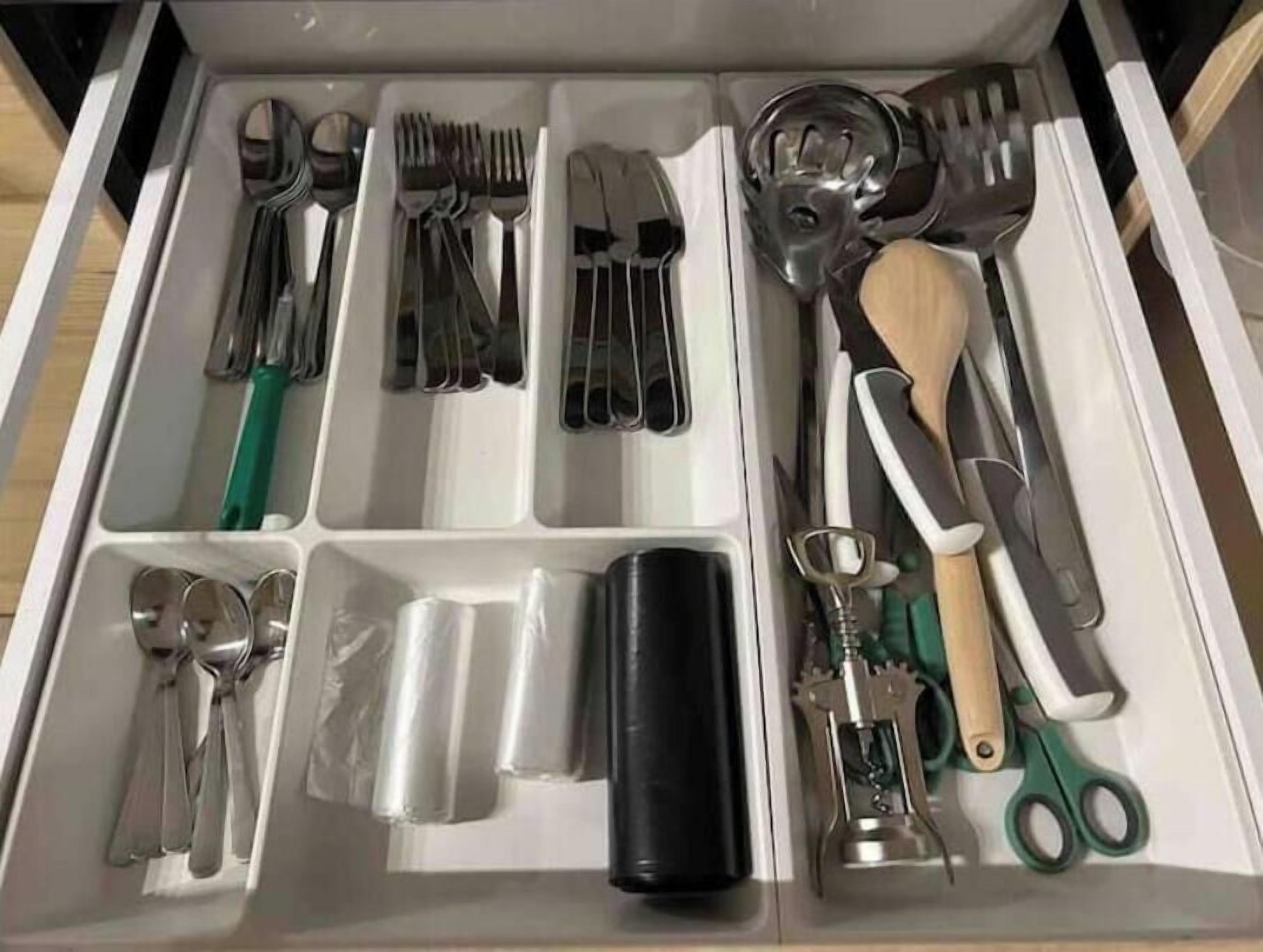 Un cajón con separadores que contiene varios utensilios de cocina como tenedores, cucharas y un rallador.