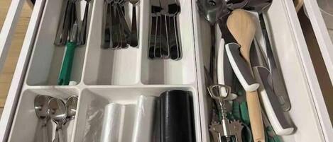 A drawer with compartments containing various kitchen utensils like forks, spoons, and a grater.