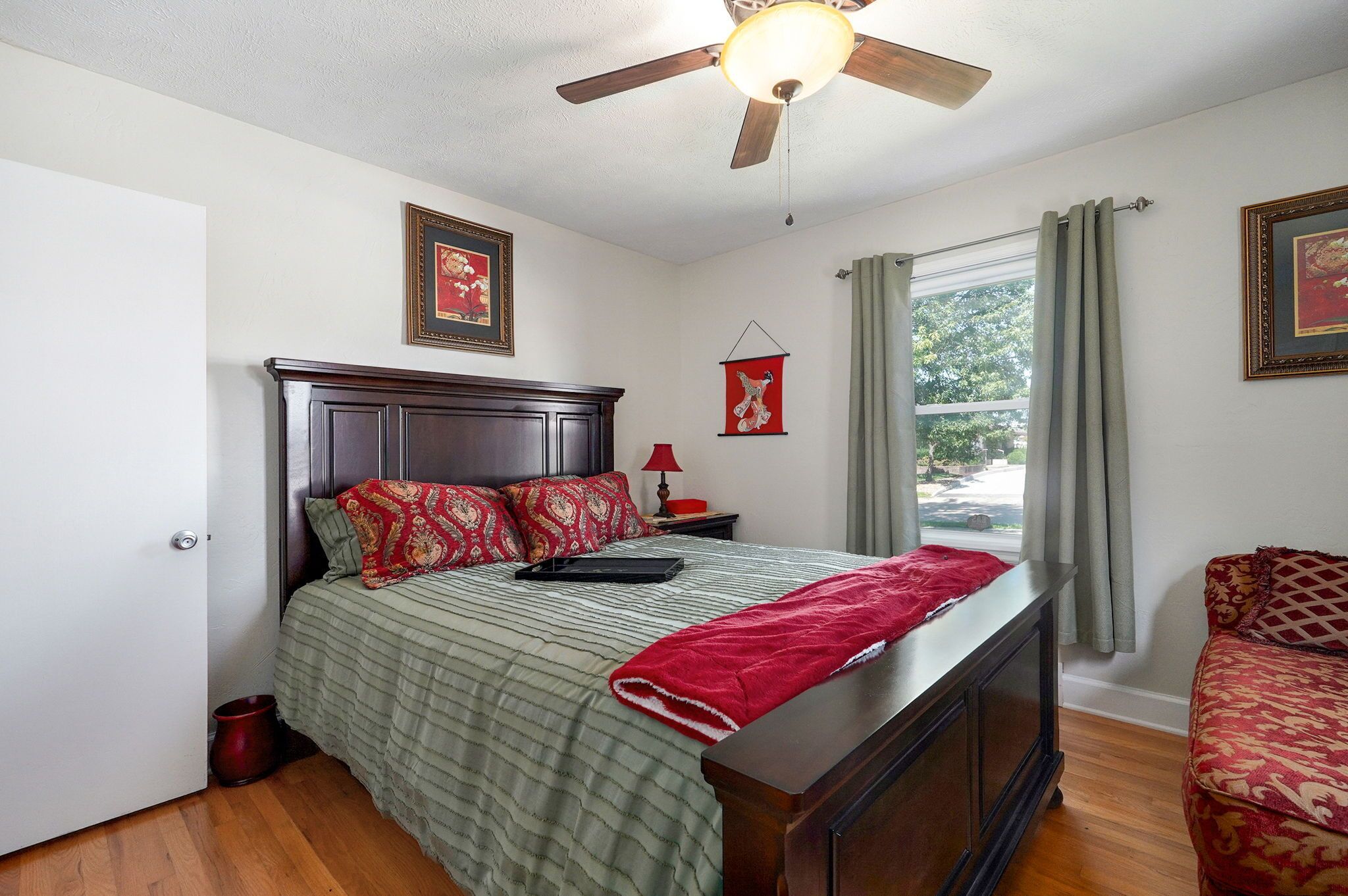 A neatly arranged bedroom with a bed, a nightstand, a red lamp, and a window with curtains.