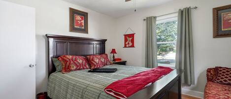 A neatly arranged bedroom with a bed, a nightstand, a red lamp, and a window with curtains.