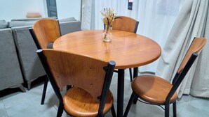 Een ronde houten eettafel met vier stoelen, een vaas met gedroogde bloemen en een grijze bank op de achtergrond.