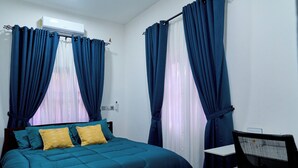 Een slaapkamer met een bed, twee kussens, een stoel en gordijnen.