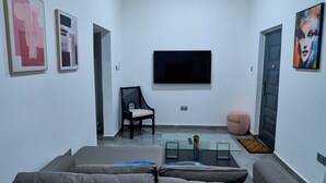 Een woonkamer met een bank, een glazen salontafel, een aan de muur bevestigde televisie en kunstwerken aan de wanden.
