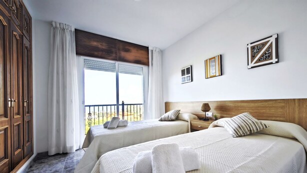 Une chambre d’hôtel avec deux lits, une grande fenêtre avec des rideaux, une tête de lit en bois et une vue sur l’extérieur.