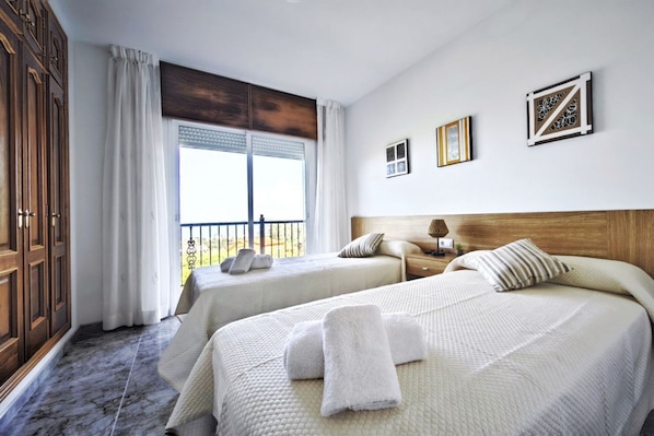 A hotel room with two beds, a large window with curtains, a wooden headboard, and a view of the outdoors.