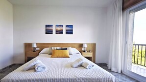 Une chambre d’hôtel avec un grand lit, deux tables de chevet avec des lampes, une tête de lit en bois et un balcon avec vue.