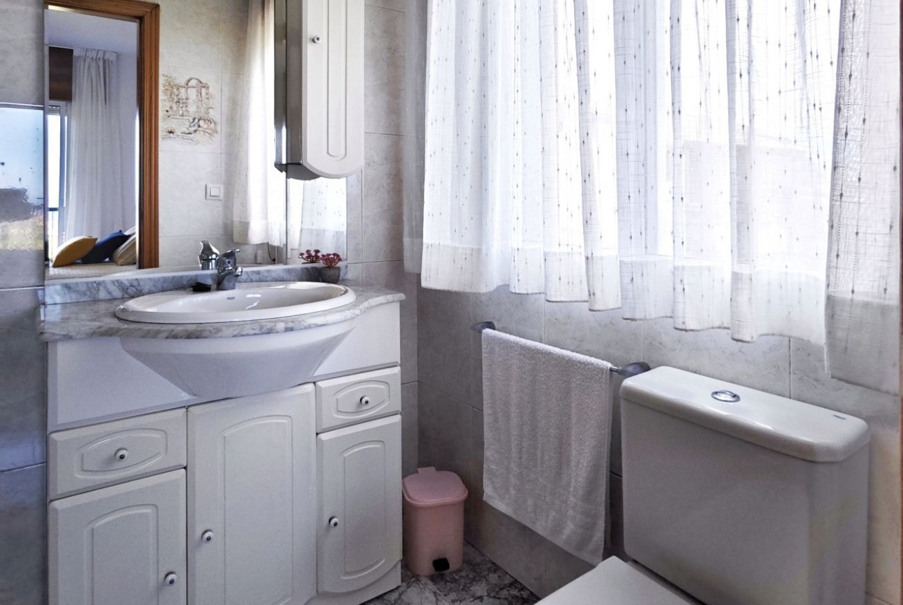 Une salle de bain équipée d’un lavabo, d’un miroir, d’un meuble de rangement, de toilettes et d’une petite poubelle.