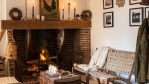 Una sala de estar acogedora con chimenea de ladrillo, un sillón tejido, un banco de madera y una mesa con velas.