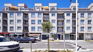 Un edificio residencial de varios pisos con balcones, un paso de peatones y coches estacionados.