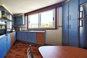 Une cuisine avec des meubles de couleur bleue, une hotte de cuisinière en acier inoxydable, une fenêtre et un coin repas.