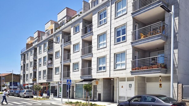 Un edificio residencial de varios pisos con balcones, un paso de peatones y automóviles estacionados.