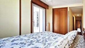 Un dormitorio con cama, un armario de madera, una puerta y una ventana.