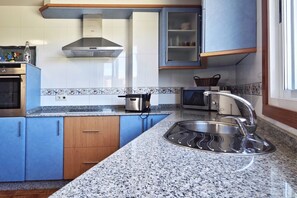 A kitchen with blue cabinets, a stainless steel sink, a microwave, and a stove.