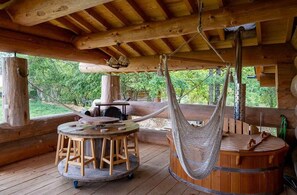 Een houten terras met een ronde tafel en stoelen, een hangmat en een houten kuip.