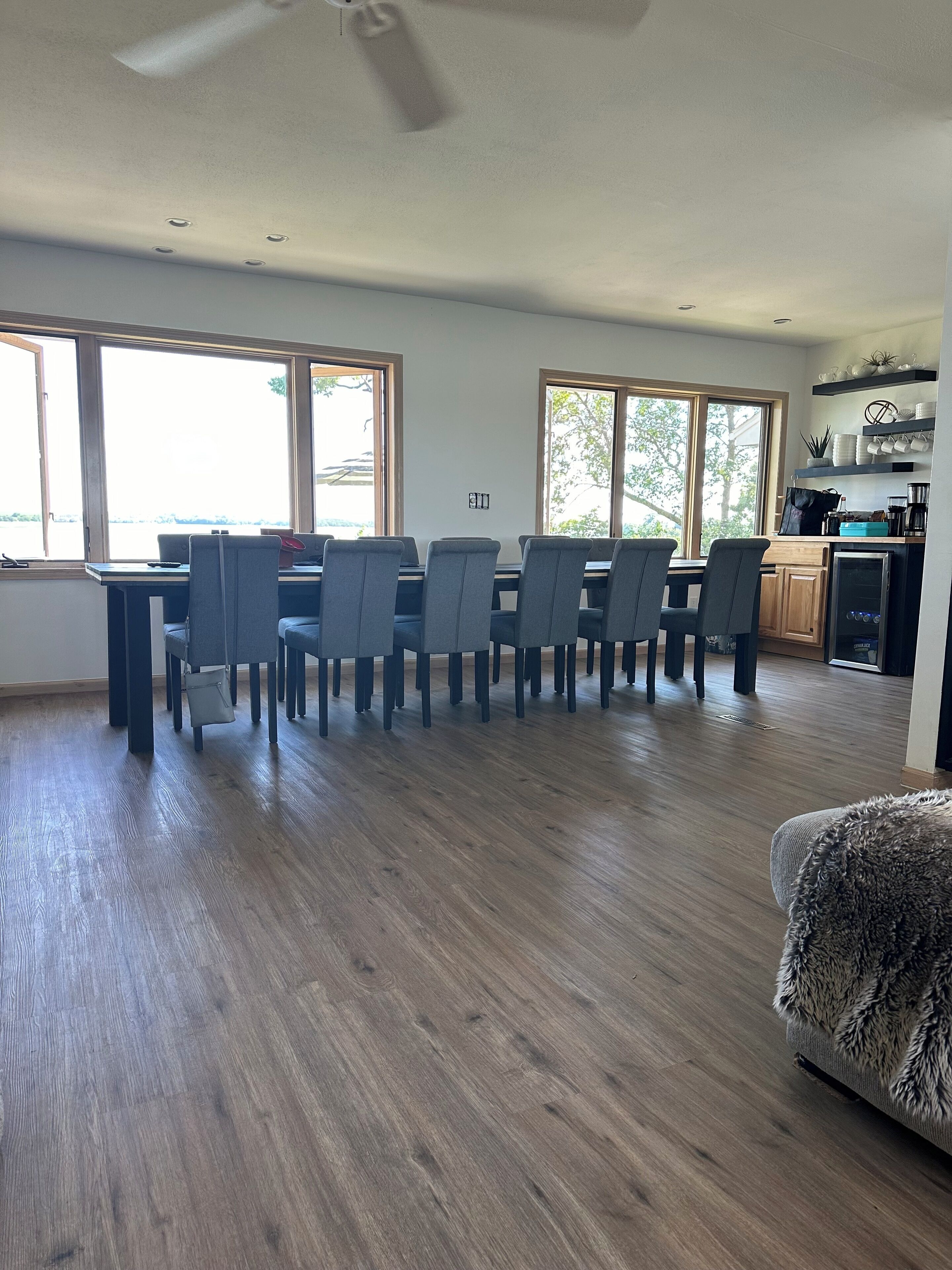 Een ruime woonkamer met een eettafel en stoelen, grote ramen en een keuken.