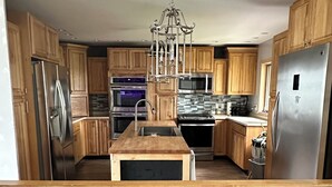 Een moderne keuken met houten kasten, roestvrijstalen apparatuur en een centraal eiland met een kroonluchter.
