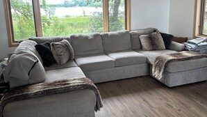 Een moderne woonkamer met een hoekbank, grote ramen en een plafondventilator.