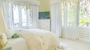 Une chambre à coucher comprenant un lit, une commode, un téléviseur et donnant sur l’extérieur.