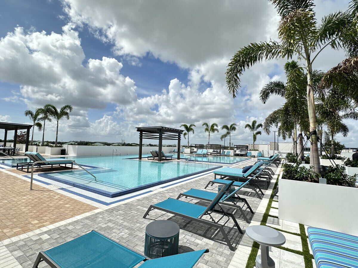 A poolside area with lounge chairs, a pergola, and palm trees.