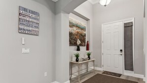 Un couloir avec un mur gris, une citation inspirante encadrée, un tableau, une porte et une petite table sur laquelle sont posées des plantes en pot.