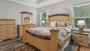 Une chambre à coucher comprenant un lit, deux tables de chevet, une commode, un miroir et une fenêtre avec des stores.