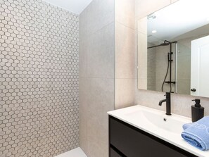 Une salle de bain avec un mur recouvert de carreaux hexagonaux, un lavabo blanc avec un robinet noir, un meuble noir et une serviette posée sur le comptoir.