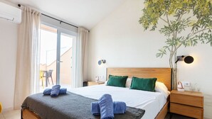 A bedroom with a large bed, a nightstand, a wall-mounted lamp, and a view of the outside balcony.