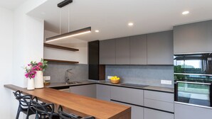 A modern kitchen with a wooden bar and black bar stools, grey cabinetry, and a built-in oven.