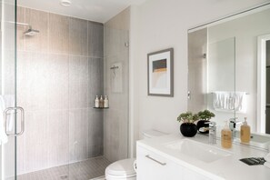 A modern bathroom with a glass-enclosed shower, a white sink, and a large mirror. - Skyline Panorama | 2BR LoHi Loft | Dog-Friendly (Denver)