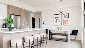 A modern kitchen with a white countertop, stainless steel appliances, and a bar stool seating area. - Skyline Panorama | 2BR LoHi Loft | Dog-Friendly (Denver)