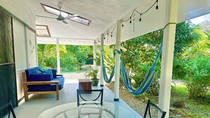 Ein überdachter Außenbereich mit einem Glastisch und Stühlen, einem blauen Sofa und einer Hängematte.
