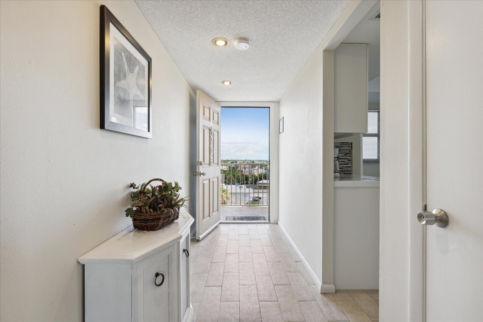 A hallway with a white door leading to a balcony with a view of buildings and cars.