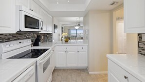 A modern kitchen with white cabinetry, a microwave, stove, and oven. There is a ceiling fan, a view of the ocean, and a dining area with a table and chairs. - Charming Oceanfront Condo with Breathtaking Views, Shuffleboard & Heated Pool! 🌊 (Cape Canaveral)