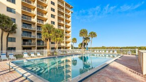 A swimming pool with lounge chairs and a high-rise building with balconies. - Oceanfront Retreat with Large Heated Pool, Private Balcony & Stunning Views!🌴 (Cape Canaveral)