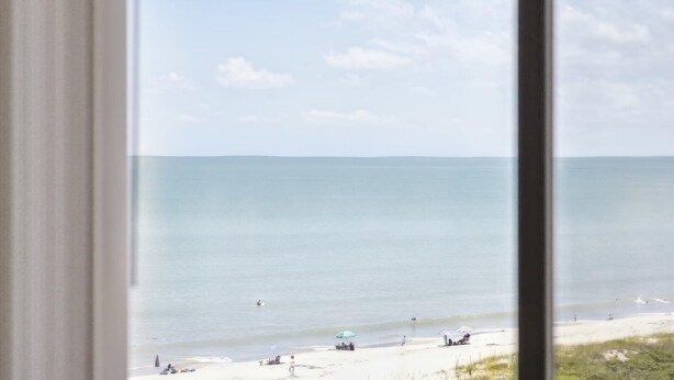A beach view through a window, with a clear sky and calm sea. - Oceanfront Retreat with Large Heated Pool, Private Balcony & Stunning Views!🌴 (Cape Canaveral)