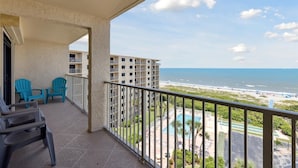 A balcony with turquoise chairs, a pool, and a view of the beach and ocean. - Spacious 3BR Corner Condo | Perfect for Groups + Ocean Views from Every Angle! 🌴 (Cape Canaveral)
