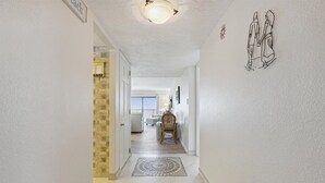 A hallway with a patterned rug, a dining area with chairs, and a ceiling light. - Spacious 3BR Corner Condo | Perfect for Groups + Ocean Views from Every Angle! 🌴 (Cape Canaveral)