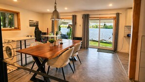 Un espace repas avec une table en bois, des chaises et une vue sur un lac, visible à travers de grandes portes vitrées.