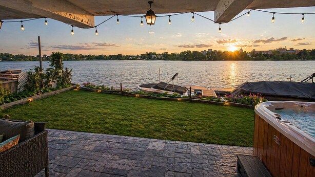 Une terrasse dotée d’un jacuzzi, d’un espace salon extérieur et offrant une vue sur un lac au coucher du soleil.