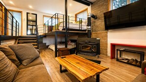 Un intérieur moderne avec une chambre à coucher aménagée en mezzanine, une table en bois, un canapé et une cheminée.