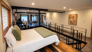 Une chambre à coucher avec un lit, un balcon doté d’une balustrade, un tableau accroché au mur et une vue sur une étendue d’eau.