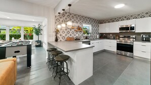 Eine moderne Küche mit einer zentralen Kochinsel, Barhocker, einem Kicker und einem großen Fenster.