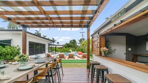 Eine überdachte Terrasse mit Holztisch und -stühlen, einem Pool und einer Bar.