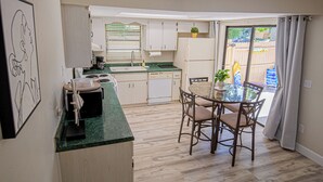Cocina compacta con zona de comedor, con encimera verde, armarios de madera y una mesa con sillas.