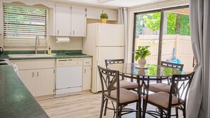 Una cocina con una mesa de comedor y sillas, un refrigerador y una ventana con persianas.