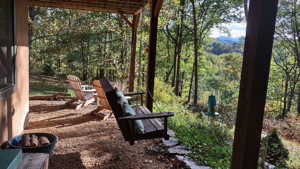 Un espace extérieur aménagé, abrité et doté de chaises Adirondack et d’une balançoire, le tout entouré d’un paysage boisé.