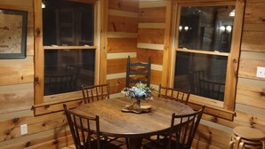 L’intérieur d’un chalet en bois présente une table à manger ronde entourée de chaises, un luminaire suspendu et de grandes fenêtres.