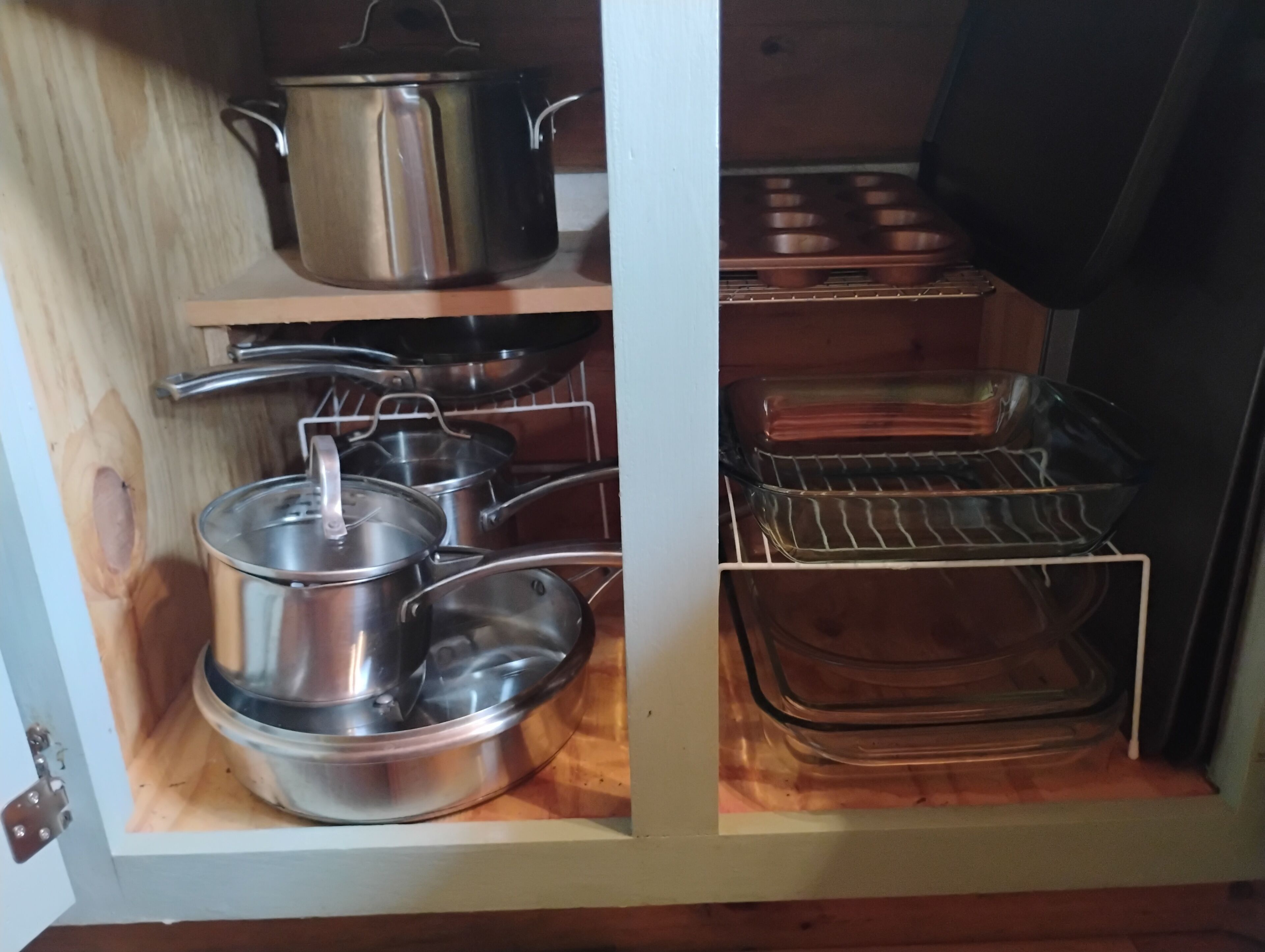 A kitchen cabinet with stainless steel cookware and glass baking dishes.